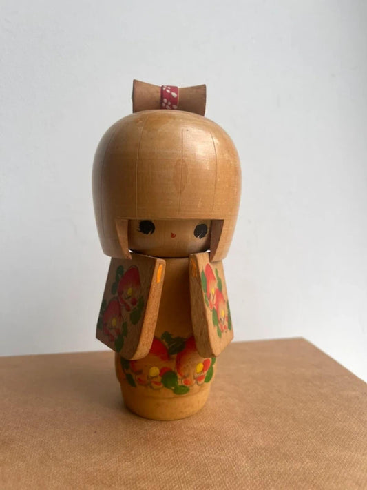 Vintage Japanese Kokeshi doll with hand-painted peach kimono and red bow, traditional wooden folk art figurine, collectible Japanese home decor, handcrafted display ornament and unique cultural gift.